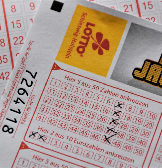 A close-up image of lottery tickets featuring crossed-out numbers, brand logos, and various numbers in a grid format. The tickets have sections for different games, and numbers are marked with black crosses.